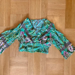 Croppad grön paisley blus - Croppad omlott topp/blus från new yoker i grönt med paisley mönster, stl XS. Tröjan är aldrig använd och är därför i nyskick. Klicka gärna på köp nu och meddela för eventuella frågor. :)
