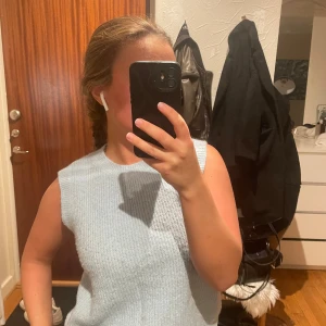 Ljusblå ärmlös topp - Säljer en superfin ljusblå ärmlös topp i stickat material. Perfekt för sommardagar eller som ett lager under en jacka. Toppen har en enkel och stilren design som gör den lätt att matcha med olika outfits. Passar både till vardags och fest!