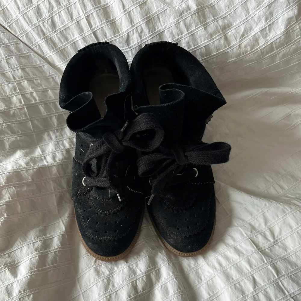 Säljer ett par snygga svarta sneakers från Isabel Marant i storlek 39. De är gjorda i mocka och har en cool kilklack för extra höjd. Skorna har snörning framtill och en bekväm gummisula. Perfekta för både vardag och fest!. Skor.