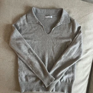Grå tröja från Design Si - Grå stickad tröja från Design Si. Den är i bra skick och har en krage med v-ringning.  Tröjan är mjuk och bekväm, med ribbade muddar vid ärmslut och nederkant. Nästintill oanvänd!