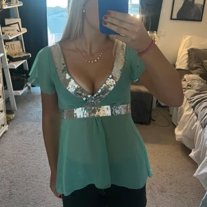 Turkos topp med paljettdetaljer - Säljer en superfin turkos topp med glittriga paljettdetaljer runt halsringningen och midjan. Toppen har korta ärmar och en v-ringad design som ger en festlig look. Perfekt för sommarens fester eller en utekväll! 💙 hör av er om fler bilder💕