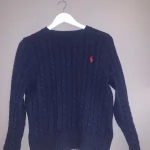 Säljer en snygg mörkblå stickad tröja från Polo Ralph Lauren. Jag säljer den då den är för liten nu, men har använt den försiktigt. Den har ett klassiskt flätmönster och den ikoniska röda loggan på bröstet. Perfekt för kyliga dagar och ger en stilren look. Passar både till vardags och lite finare tillfällen. Inga synliga skråmor eller fläckar. Storlek small pris 700 köpt för 1700 pris kan diskuteras. Kom Dm för mer bilder