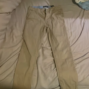 Beige byxor från H&M - Säljer ett par beige byxor från H&M i storlek 158. De är i bra skick och perfekta för vardagsbruk. Byxorna har en klassisk stil med dragkedja och knapp framtill. Passar bra till både skola och fritid!