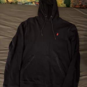 Svart hoodie från MCS - Säljer en stilren svart hoodie från MCS i storlek S. Den har en klassisk design med en liten röd logga på bröstet och en praktisk magficka. Perfekt för både vardag och chill. Huvan har dragsko för justerbar passform. Skön och enkel att matcha med det mesta!