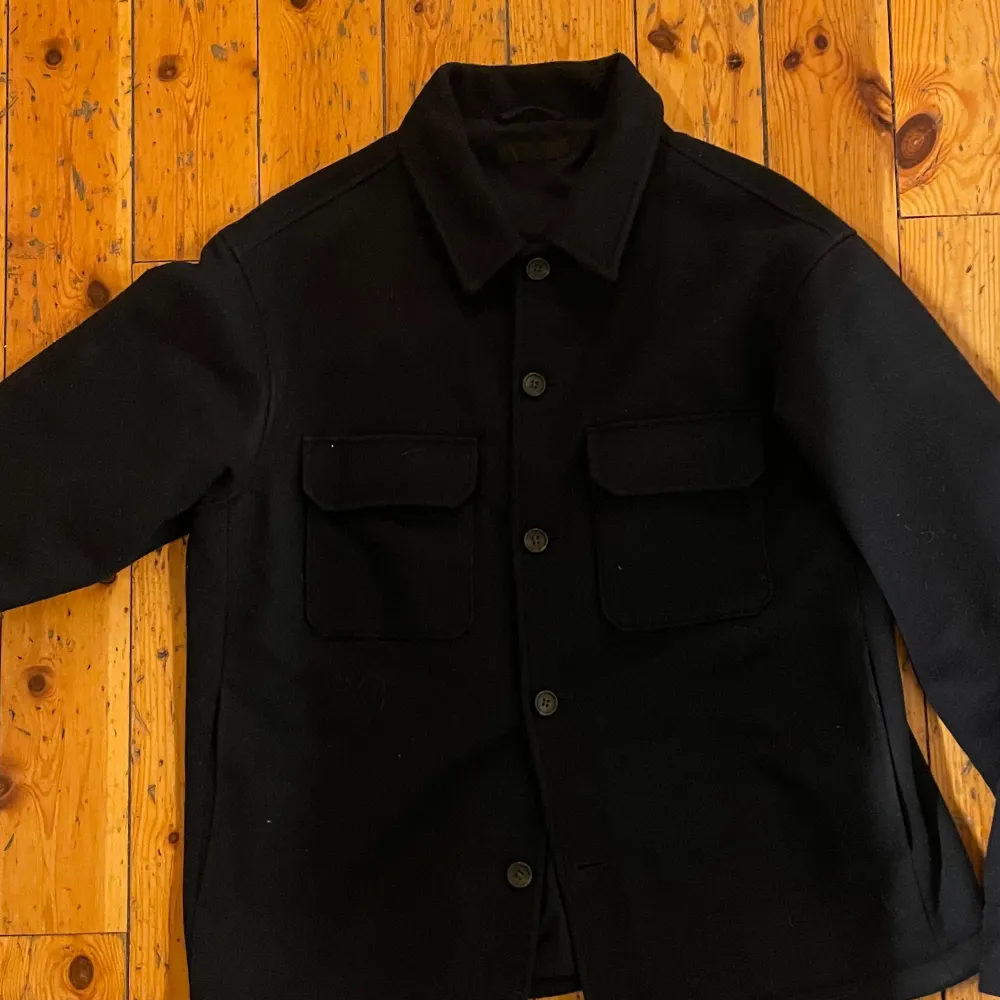 Säljer en stilren svart overshirt i bra skick. Den har långa ärmar och knappar framtill, perfekt för höst och vinter då den också är fodrad. Två praktiska bröstfickor ger en cool look. Passar både till vardags och lite mer uppklädda tillfällen. Perfekt för lager-på-lager-stilen! Köpt för 1800. Jackor.