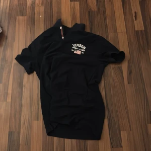 Svart pikétröja från Vinson Polo Club - Säljer en snygg svart pikétröja från Vinson Polo Club. Den har en klassisk design med knappar och ett broderat märke på bröstet. Perfekt för en avslappnad men stilren look. Passar bra till både vardag och fest!