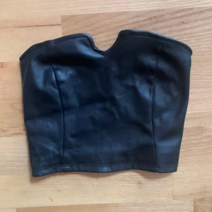 Svart tubtopp i skinnimitation - Snygg svart tubtopp i skinnimitation, perfekt för en utekväll. Toppen har en tight passform och en elastisk baksida för extra komfort.