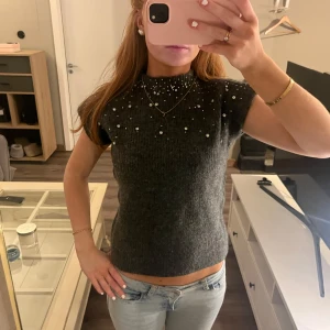 Grå stickad topp med pärlor - Säljer en stilren grå stickad topp med pärldetaljer. Toppen har en tight passform och korta ärmar, perfekt för en elegant look. Passar bra till både jeans och kjol. Perfekt för höst och vinter! Storlek xs💞💞
