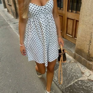 Vit prickig klänning från Zara - Säljer en söt vit klänning med svarta prickar från Zara. Klänningen har en v-ringad design och är ärmlös, perfekt för sommardagar. Den har en luftig passform som ger en bekväm känsla. Perfekt för en dag på stan eller en sommarfest! 🌼