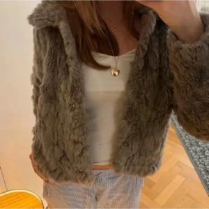 Grå pälsjacka  - Säljer en mysig grå pälsjacka med knappar framtill. Jackan har en fluffig och varm känsla, perfekt för kyligare dagar. Den är kort och har långa ärmar, vilket ger en trendig look.