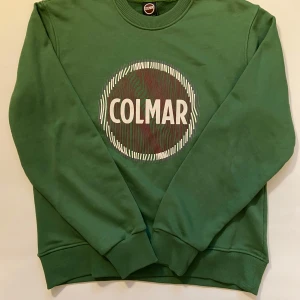 Grön sweatshirt från Colmar - Snygg grön sweatshirt från Colmar med ett stort tryck på framsidan. Tröjan har långa ärmar och ribbade muddar vid ärmslut och nederkant. Perfekt för en avslappnad stil. Använd en eller två gånger.