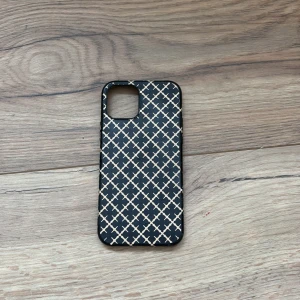 Svart mobilskal med mönster från By Malene Birger - Snyggt svart mobilskal med ett elegant rutmönster i beige från By Malene Birger. Perfekt för att ge din telefon en stilren look samtidigt som den skyddas. Passar utmärkt för dig som vill ha både stil och funktion. Till för iPhone 12.