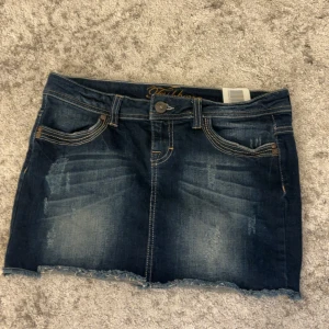Jeanskjol från Fishbone - Snygg vintage jeanskjol från Fishbone i mörkblå denim med slitna detaljer och fransig nederkant. Kjolen har klassiska femfickor och knappgylf. Perfekt för en avslappnad stil.pris kan diskuteras 