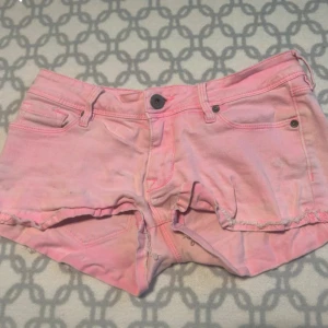 Lowwaist Rosa jeansshorts - Snygga rosa jeansshorts med låg midja och klassisk femficksdesign. Perfekta för sommardagar och festivaler. De har en knapp och dragkedja framtill.