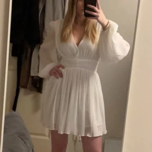 Vit klänning från NA-KD - Säljer en super fin vit klänning från NA-KD med v-ringning och långa ärmar. Klänningen har en öppning i ryggen och ett fint fall som ger en luftig känsla. Perfekt för sommaren och t.ex. studenten☺️☀️