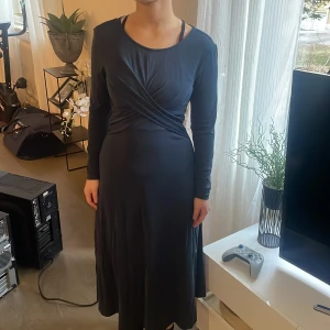 Mörkblå långärmad klänning - Elegant mörkblå klänning med omlottdetalj framtill. Den har långa ärmar och en smickrande passform som passar perfekt för höst och vinter. Klänningen är tillverkad i ett mjukt och bekvämt material.