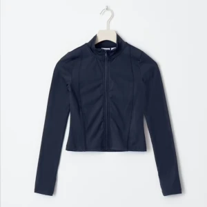 Mörkblå tight jacka med dragkedja - Snygg mörkblå jacka med dragkedja framtill. Jackan har en tight passform och långa ärmar, perfekt för en stilren look. Den är tillverkad i ett mjukt och stretchigt material som ger komfort och rörelsefrihet. Pris kan diskutera