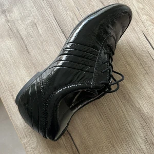 Svarta lackskor från Ecco - Snygga svarta lackskor från Ecco med elegant snörning. Skorna har en glansig yta och en stilren design som passar perfekt för en chic look. Perfekta för att ge en touch av elegans till din outfit på jobbet. 