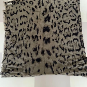 Leopardmönstrad militärgrön scarf från By Malene Birger - Snygg leopardmönstrad scarf från By Malene Birger i en militärgrön/svart färgkombination. Perfekt för att ge din outfit en trendig touch. Halsduken är mjuk och lätt, vilket gör den idealisk för både höst och vår. Någon tråddragning men inget som syns när man bär den (därav priset). 