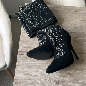 Svarta stövletter med strassdetaljer - Snygga svarta stövletter med hög klack och spetsig tå. Dekorerade med glittrande strass som ger en lyxig känsla. Perfekta för att sätta en glamorös touch på din outfit.
