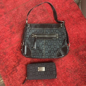 Mönstrad axelväska och plånbok från Vezzano - Snygg axelväska och matchande plånbok från Vezzano med geometriskt mönster. Väskan har en praktisk dragkedja framtill och justerbar axelrem. Plånboken har en metallplatta med logotyp och dragkedja (lite sliten) Perfekt för att hålla ordning på dina saker med stil!