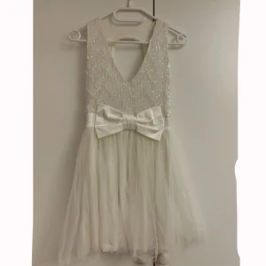 Vit glittrig klänning med rosett - Säljer en supersöt vit klänning med glittrig överdel och stor rosett i midjan. Klänningen har en v-ringad design framtill och en öppen del i ryggen. Kjolen är av tyll och lagom fluffig. Perfekt för speciella tillfällen eller som studentklänning! ✨Storleken är 36/S men skulle säga att den är liten och kort i storleken så passar mer XS/S. Bra skick.