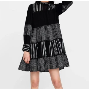 Svart och vit randig klänning - Trendig svart och vit randig klänning med lång ärm och volangdetaljer. Perfekt för en stilfull look med sin lösa passform och korta längd. Klänningen har ett unikt mönster som ger en modern touch.