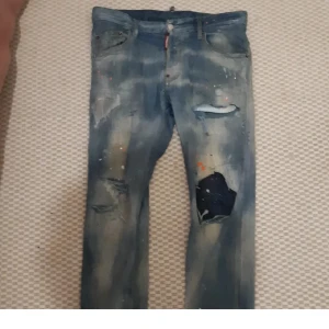 Blå jeans från Dsquared2 - Snygga blå jeans från Dsquared2 med slitna detaljer och färgstänk för en edgy look. De har en klassisk femficksdesign och knappgylf. Perfekta för dig som vill ha en unik stil.