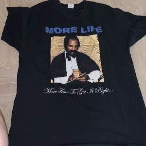 Svart t-shirt med tryck från Gildan Drake merch - Säljer en svart t-shirt från Gildan med ett stort tryck på framsidan. Texten 'MORE LIFE' och 'More Time To Get It Right...' finns ovanför och under bilden. Perfekt för en avslappnad stil.