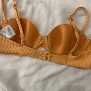 Orange ribbad bikiniöverdel från H&M - Snygg orange bikiniöverdel från H&M med ribbad textur. Den har justerbara axelband och en klassisk bygel för extra stöd. Perfekt för soliga dagar på stranden eller vid poolen.