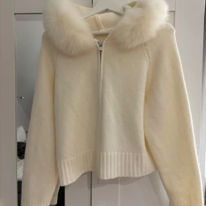 Alessa fur jacket - Säljer en superfin vit stickad jacka med fluffig pälskrage och dragkedja framtill från alessa. Jackan har en mysig huva och långa ärmar. Perfekt för kyliga dagar när du vill vara både varm och stilren. Passar xs/s