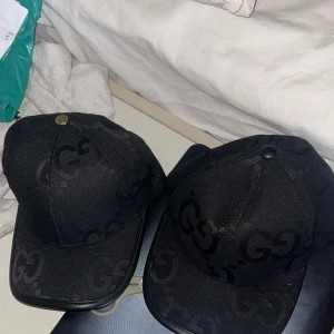 Svart keps från Gucci - Snygg svart keps från Gucci med det ikoniska GG-mönstret. Kepsen har en justerbar rem baktill med Gucci-logotypen. Perfekt för att ge en lyxig touch till din outfit.