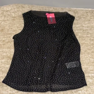 Svart glittrig ärmlös topp från Edikted  - Säljer en svart ärmlös topp från Edikted med glittriga detaljer. Perfekt för en kväll ute. Toppen har en elegant design med små glittrande prickar/stenar över hela ytan. Originalpris 565.
