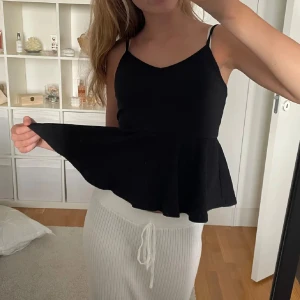 Svart ärmlös topp - Snygg svart ärmlös topp med smala axelband och volangdetalj i nederkant. Perfekt för en stilren look.