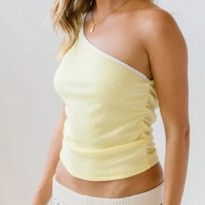 Gul oneshoulder topp från shein - Snygg gul oneshoulder topp med ribbad textur och vit kantdetalj. Perfekt för varma dagar med sin lätta och bekväma passform. Är S men passar Som M! 