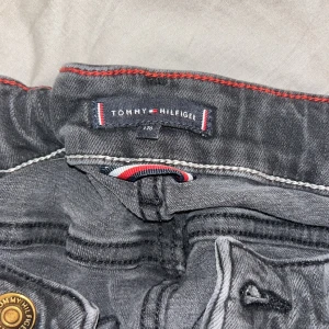 Svarta jeans från Tommy Hilfiger - Snygga svarta jeans från Tommy Hilfiger med klassisk femficksdesign. De har en dragkedja och knapp framtill samt märkets logotyp på baksidan. Perfekta för en stilren look.