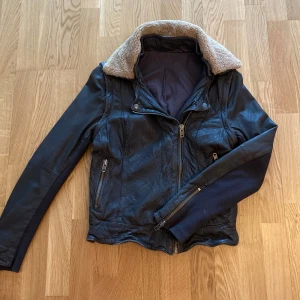 Svart skinnjacka med foder - Snygg svart skinnjacka med mjukt foder i kragen. Jackan har dragkedja framtill och på fickorna, samt långa ärmar. Perfekt för kyligare dagar med sin stilrena design och bekväma passform. Knappt använt!
