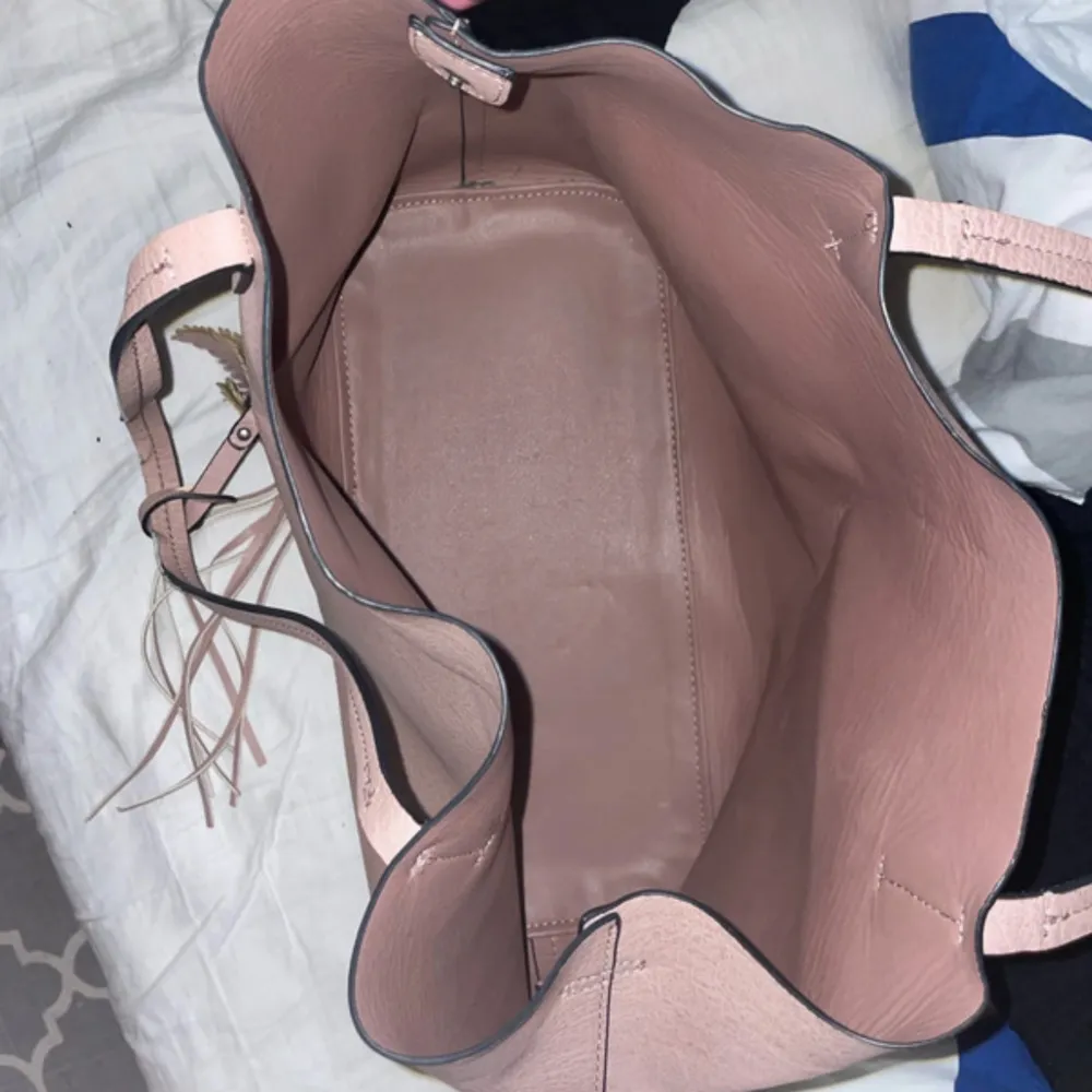 Snygg rosa axelväska i syntetmaterial med en cool fjäderdetalj och fransar. Väskan har en praktisk dragkedja och gott om utrymme för dina saker. Perfekt för att ge din outfit en extra touch!. Laukut & Käsilaukut.