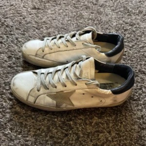 Vita sneakers med stjärndetalj - Snygga vita sneakers med en grå stjärna på sidan och svarta detaljer vid hälen. Skorna har snörning och en klassisk design som passar perfekt till vardagsstilen.