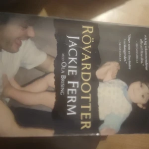Rövardotter - Boken 'Rövardotter' av Jackie Ferm med Ola Brising. Omslaget visar en bild av en vuxen och ett barn. Titeln är tryckt i stora gula bokstäver mot en mörk bakgrund.