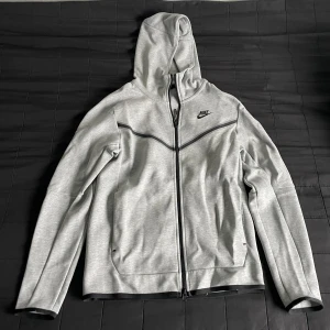 Nike tech fleece - Säljer en grå tech fleece från Nike i nyskick. Den har en dragkedja framtill och en justerbar huva. Perfekt för träning eller vardagsbruk. Den är långärmad och har en normal passform. Superbekväm och stilren design! KAN SÄNKA PRISET VID SNABB AFFÄR!!!!