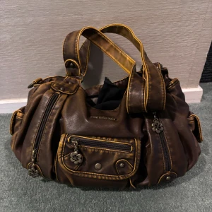 Unik brun väska  - Unik brun väska med fina blomdetaljer. Sömmen på en ficka inuti har spruckit, annars finns det inga fler defekter, ser rätt så ny ut! 