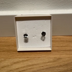 Svarta och silverfärgade örhängen - Snygga örhängen med en fyrkantig design i svart och silver. Perfekta för att ge en elegant touch till din outfit. De är små och diskreta, men ändå stilfulla. Passar både till vardags och festliga tillfällen.