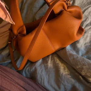 Brun axelväska i skinn - Säljer en snygg brun axelväska i skinn. Den har en stilren design med justerbar axelrem och är perfekt för vardagsbruk. Väskan är i bra skick.