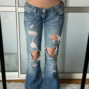 Lågmidjade bootcut jeans med hål true religion  - Super snygga jeans från true religion. Storlek 26, men enligt mig är storleken mer som en 28-29. Alldeles för stora för mig som brukar ha 26-27. Innerbenslängd: 70 midjemått:40. Köp sker via köp nu, jag postar inom 24h. Kvar tills markerad såld 
