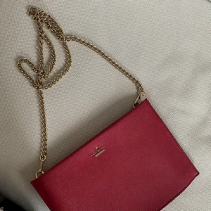 Kate Spade väska - Väska från Kate Spade i fint skick! Mörkröd/vinröd färg med guldiga detaljer.
