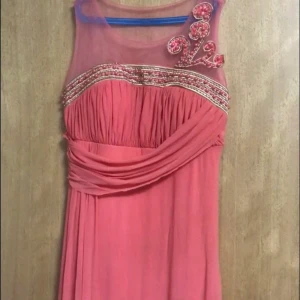 En röd rosa klänning - Klänningen är rödrosa och har pärlor som detaljer i rosa. Klänningen har rosor och har storleken 42 och kostar däremot 500kr 