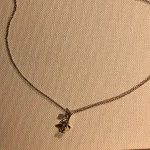 Ett guldfärgat halsband med en liten ros som berlock 