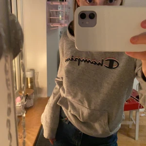 Ljus grå Champion Huddie med mörkblåa detaljer  - En helt oskadad Huddie i ett tunt material . Rekommenderad för dig som 13-14 åring, med passar mig som 16 åring , (165cm lång ) . Betalning sker via swish .