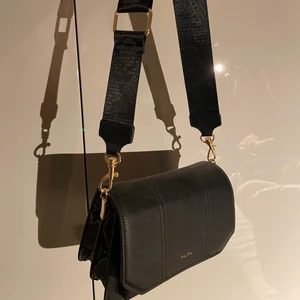 Svart väska med ormskinnsmönster - En svart väska från NA-KD med flera olika fack. Väskan är ormskinnsmönstrad på sidorna och har ett brett axelband. Aldrig använd 